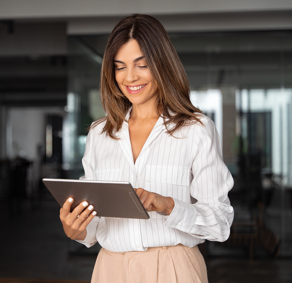 Professionally-dressed woman smiles down at tablet screen while standing in modern office space